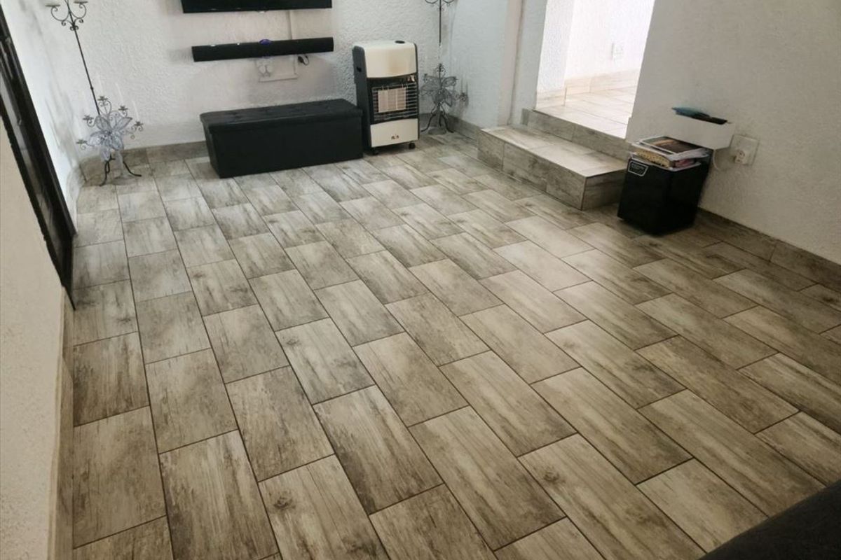 A living room area featuring modern wood-look ceramic floor tiles and a raised transition leading to an adjacent space.