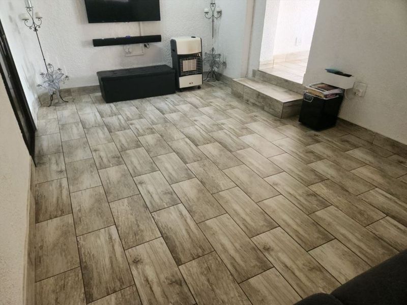 A living room area featuring modern wood-look ceramic floor tiles and a raised transition leading to an adjacent space.