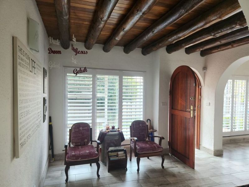 Welcoming entrance hall featuring a rustic exposed timber beam ceiling, tiled flooring, and an arched timber door with plantation shutters.