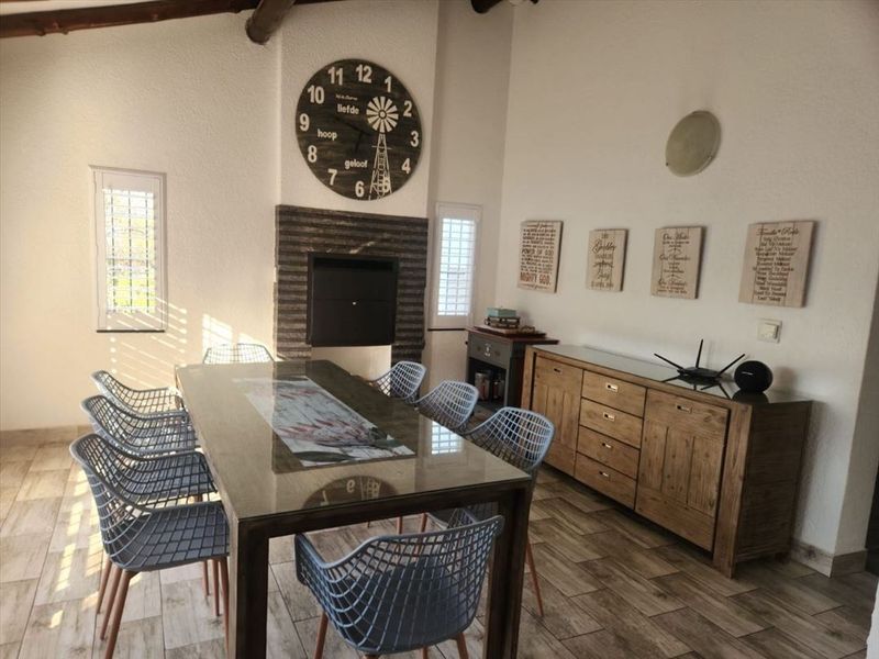A bright dining room featuring a built-in fireplace with stone surround, exposed timber ceiling beams, and modern tiled flooring.