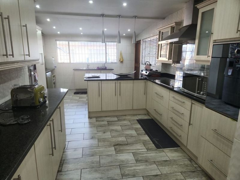 Spacious kitchen featuring light wood cabinetry, dark granite countertops, integrated oven, extractor fan, and modern tiled flooring with ample workspace.