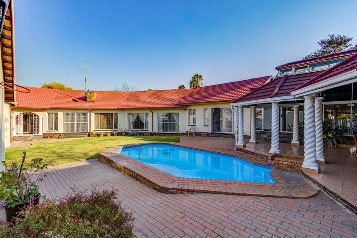 Spacious rear exterior featuring a swimming pool, brick paved patio area, and covered veranda with decorative columns, set against the main house structure.