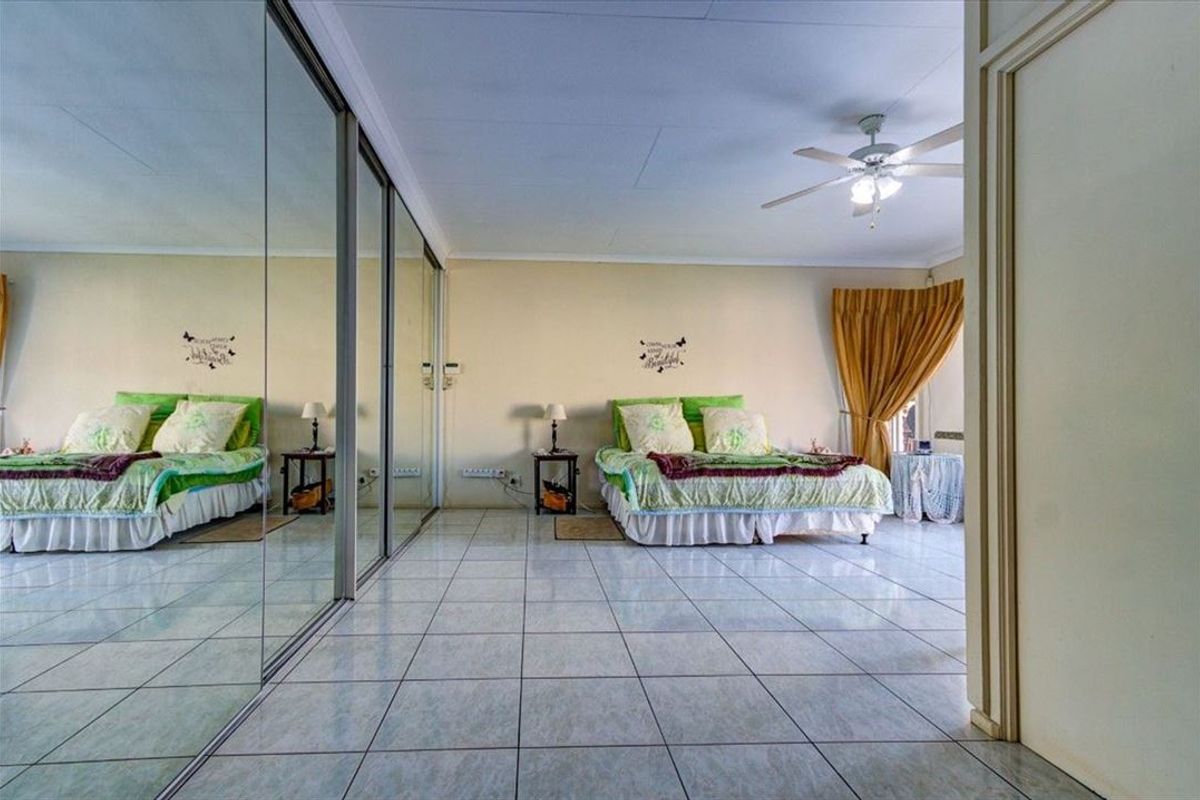 Spacious bedroom featuring large mirrored sliding wardrobe doors, tiled flooring, and a ceiling fan, offering a bright and functional living space.