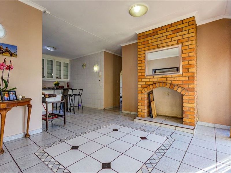 Open plan living area featuring a prominent brick fireplace and tiled flooring, seamlessly connecting to a functional kitchen space with built-in cabinetry.