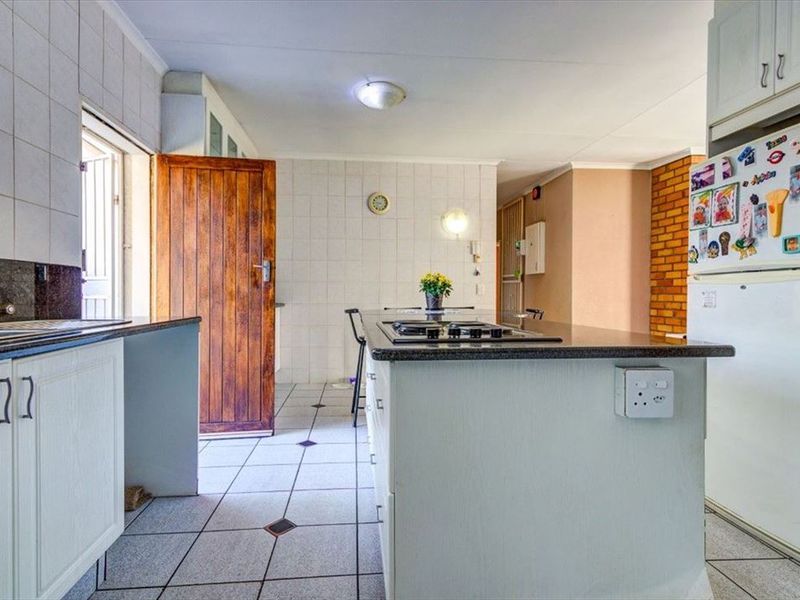 A functional kitchen featuring a central island with a built-in gas hob, granite countertops, and tiled flooring throughout.