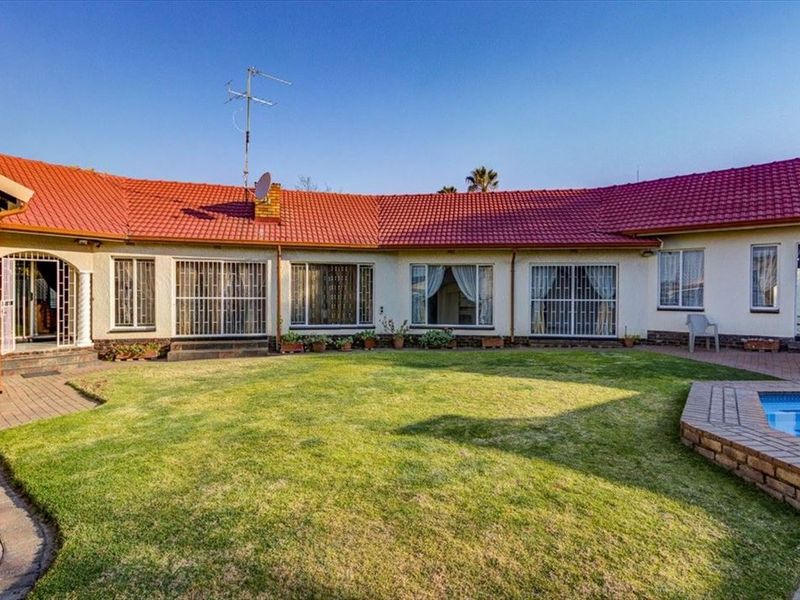 Rear view of the house featuring a red tiled roof, paved patio area, and a swimming pool set within a landscaped garden.