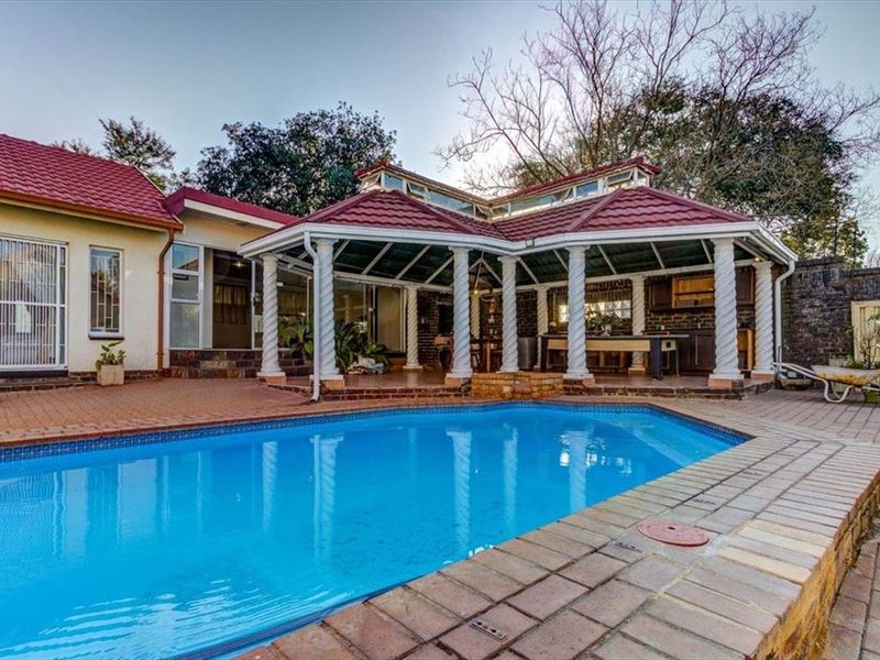 Outdoor pool area featuring a large swimming pool, paved surround, and a covered patio with structural columns and tiled roofing.