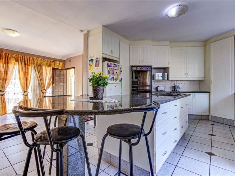 Open plan kitchen featuring a large granite island, fitted cabinetry, built-in oven, and tiled flooring, seamlessly connecting to the adjacent living area.