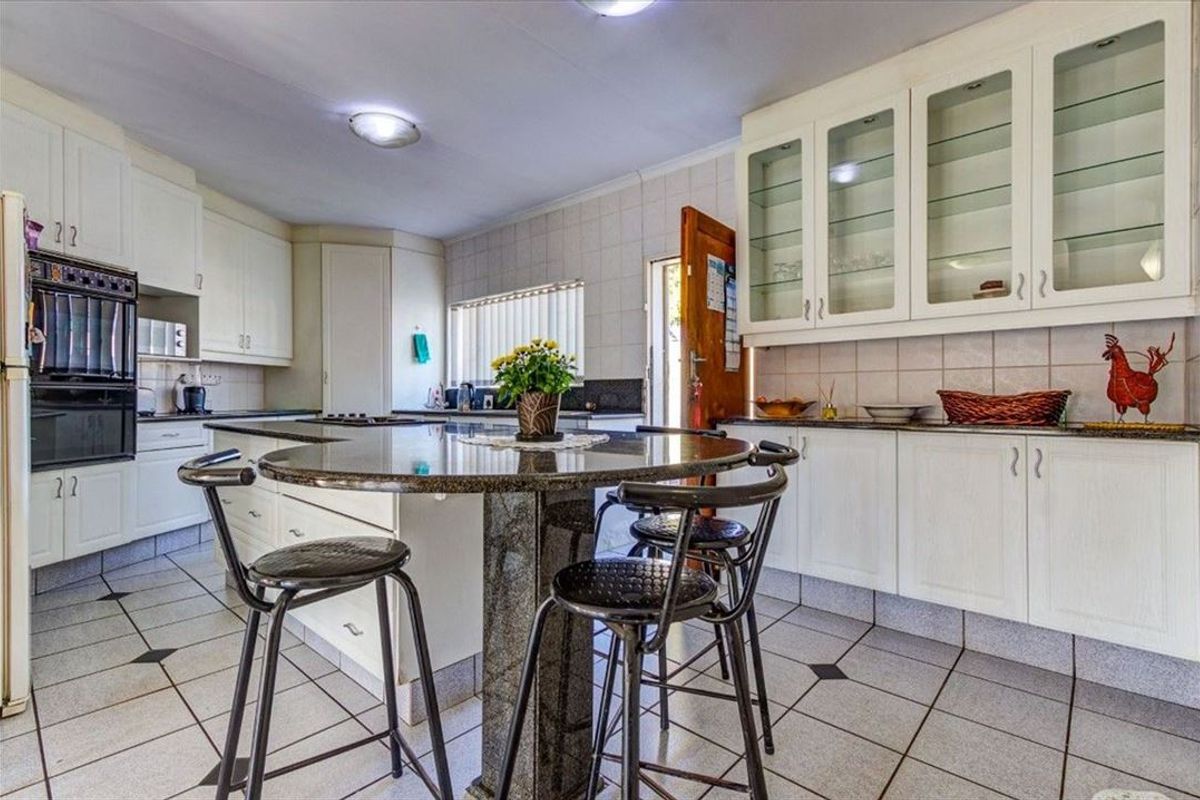 Spacious kitchen featuring white cabinetry, granite countertops, a central island with breakfast bar seating, and tiled flooring throughout.