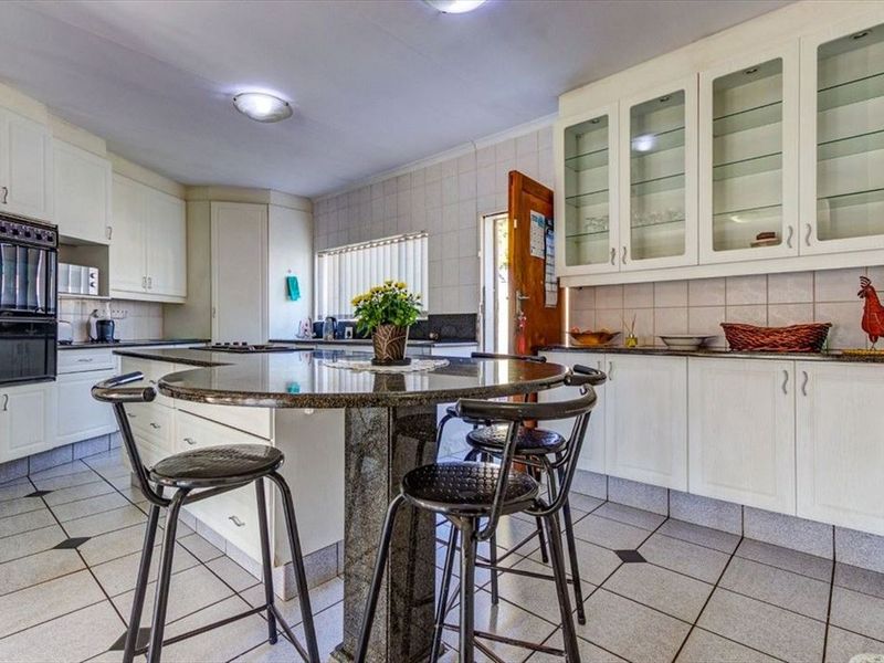 Spacious kitchen featuring white cabinetry, granite countertops, a central island with breakfast bar seating, and tiled flooring throughout.