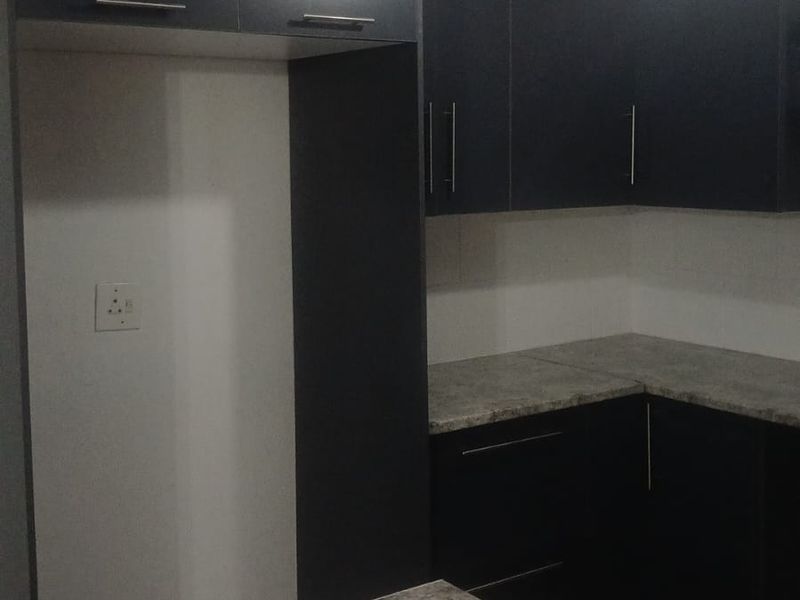 A modern kitchen featuring dark cabinetry, stone-look laminate countertops, and dedicated space for a refrigerator.