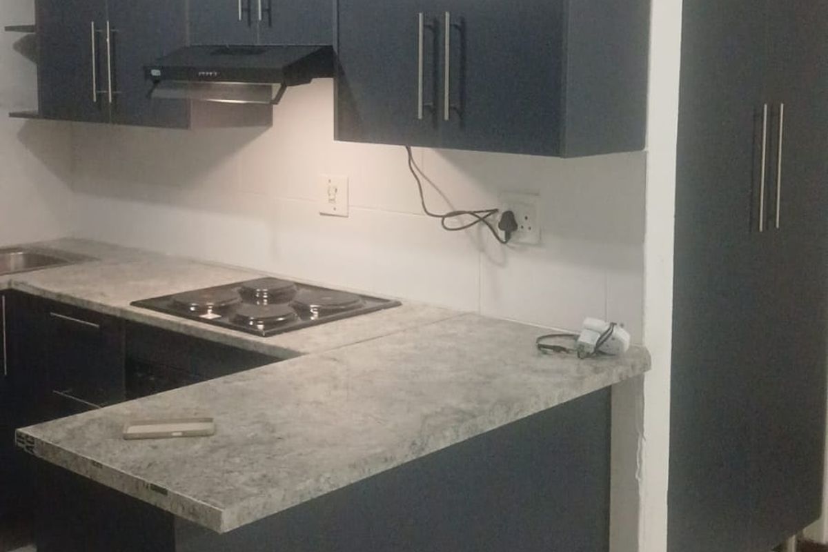 Modern kitchen featuring dark cabinetry, stone-look laminate countertops, an integrated electric hob with extractor fan, and neutral tiled flooring.