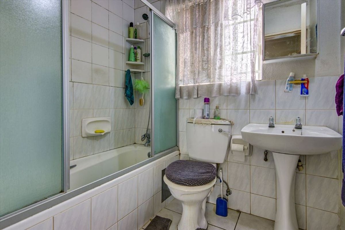 A functional bathroom featuring a pedestal basin, toilet, and a shower-over-bath combination with tiled finishes throughout.