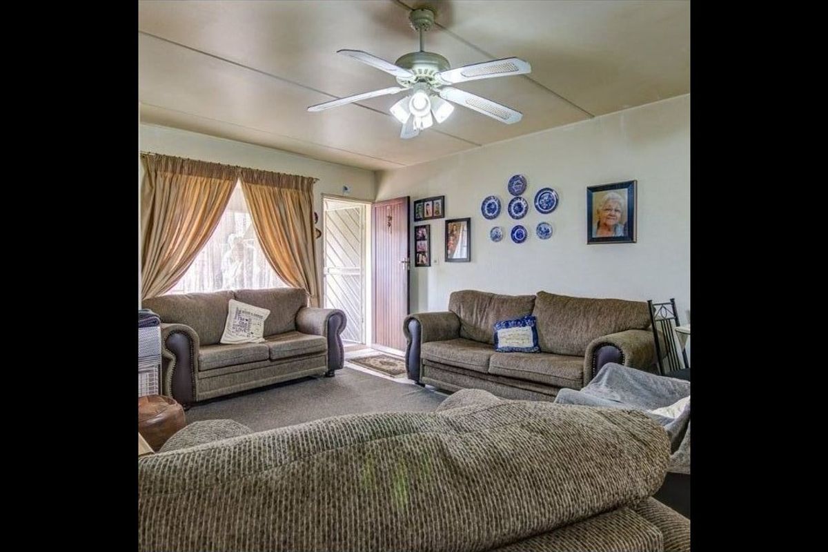 A living room featuring a ceiling fan and a security gate at the entrance, with visible wear on the ceiling panels.