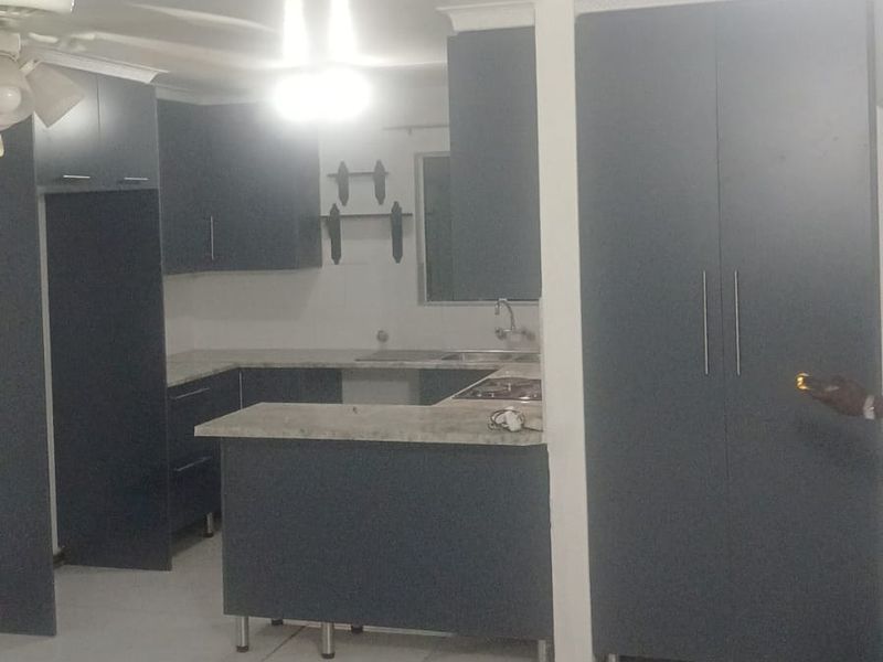 A modern kitchen featuring dark cabinetry, stone countertops, integrated hob, and tiled flooring, presented in a clean, open-plan layout.