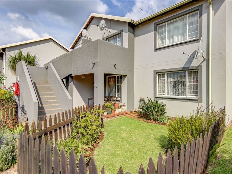 Front elevation of a two-story residential unit featuring a private garden, picket fence, and external concrete staircase leading to the upper level.
