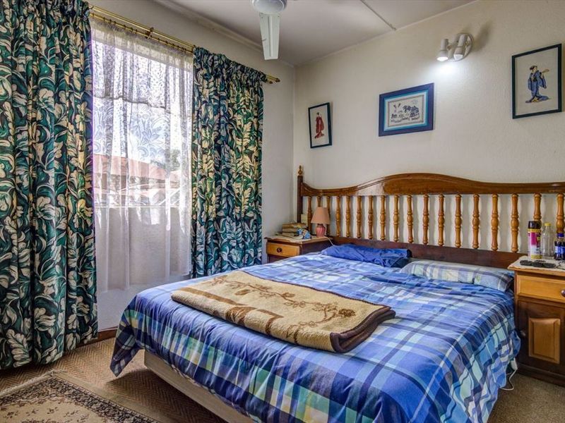 A functional bedroom featuring a ceiling fan and wall-mounted lighting, offering a comfortable space with natural light from the window.
