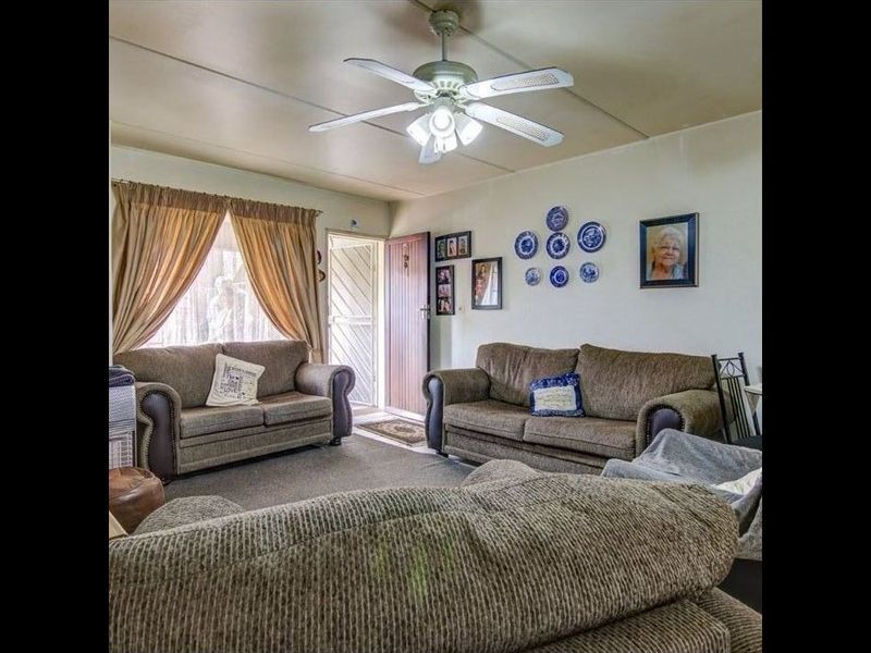 A living room featuring a ceiling fan and a security gate at the entrance, with visible wear on the ceiling panels.