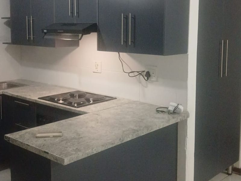 Modern kitchen featuring dark cabinetry, stone-look laminate countertops, an integrated electric hob with extractor fan, and neutral tiled flooring.
