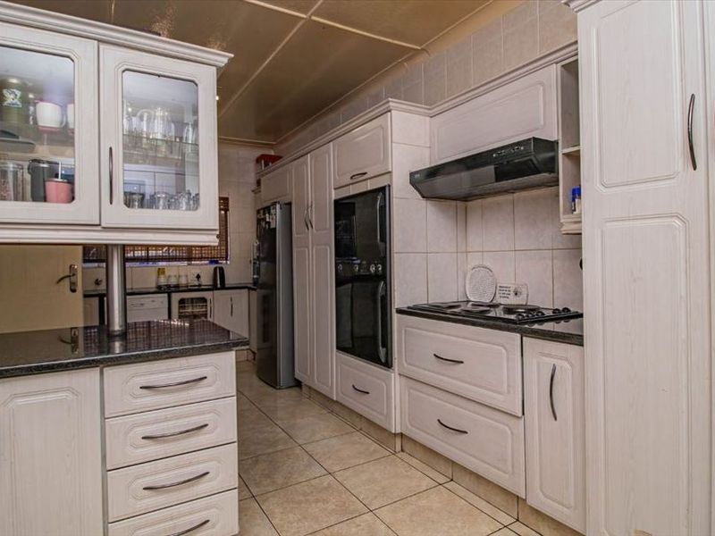 A functional kitchen featuring light-toned built-in cabinetry, granite countertops, integrated oven, hob, and extractor fan with tiled flooring and backsplash.