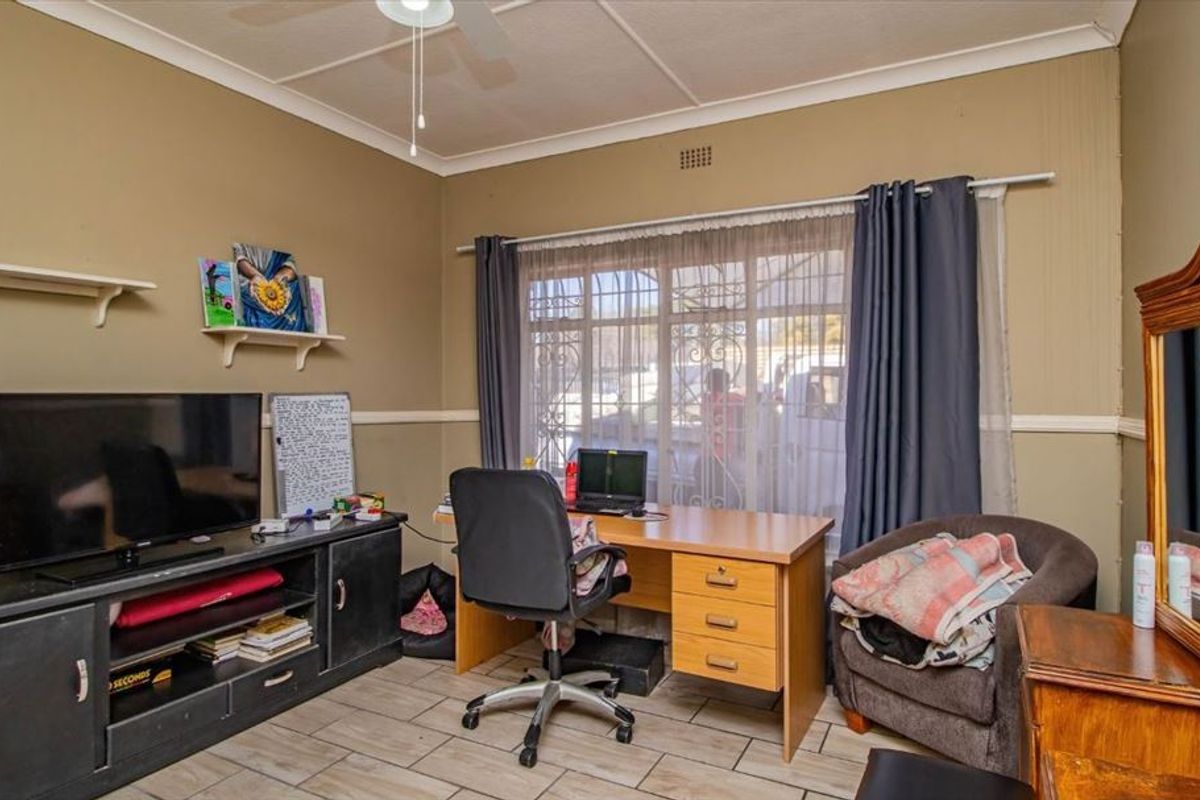 A functional bedroom featuring tiled flooring, a ceiling fan, and security bars on the window, offering a practical space for rest or study.