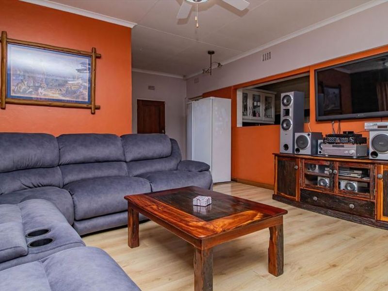 A living room featuring laminate flooring, a ceiling fan, and a pass-through window connecting to the kitchen area.