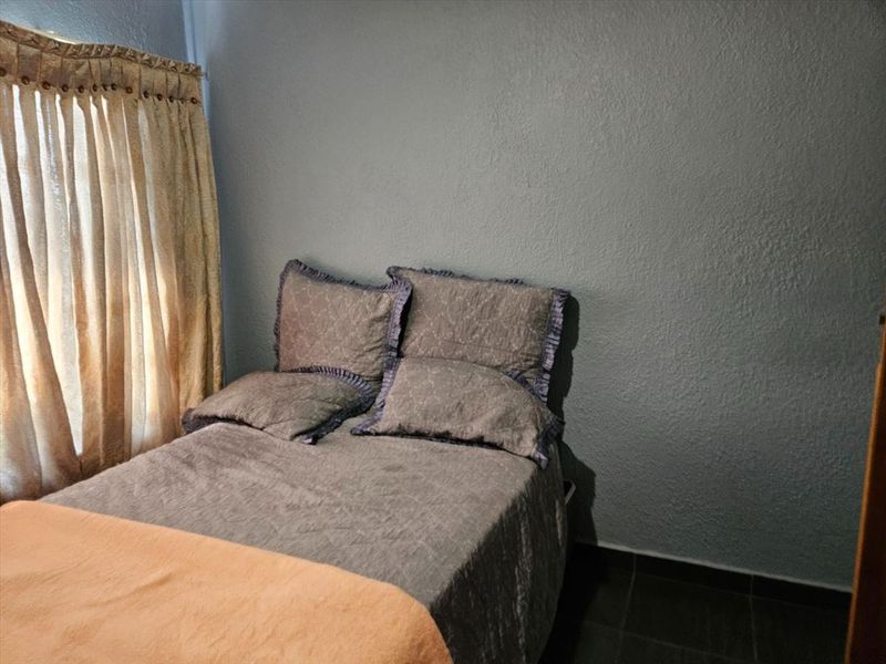 A bedroom featuring tiled flooring and a window with curtain fixtures, providing a functional space with neutral wall finishes.
