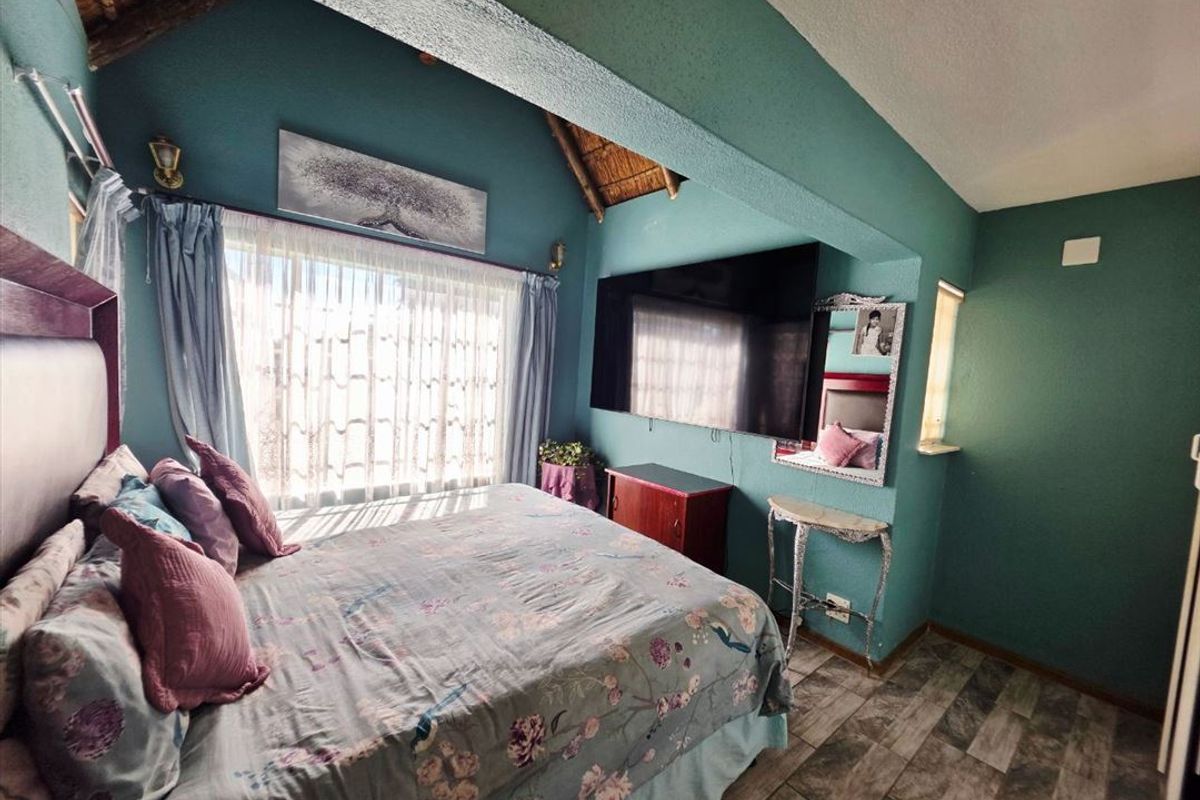 A bedroom featuring a vaulted ceiling with exposed thatch, tiled flooring, and a wall-mounted television.
