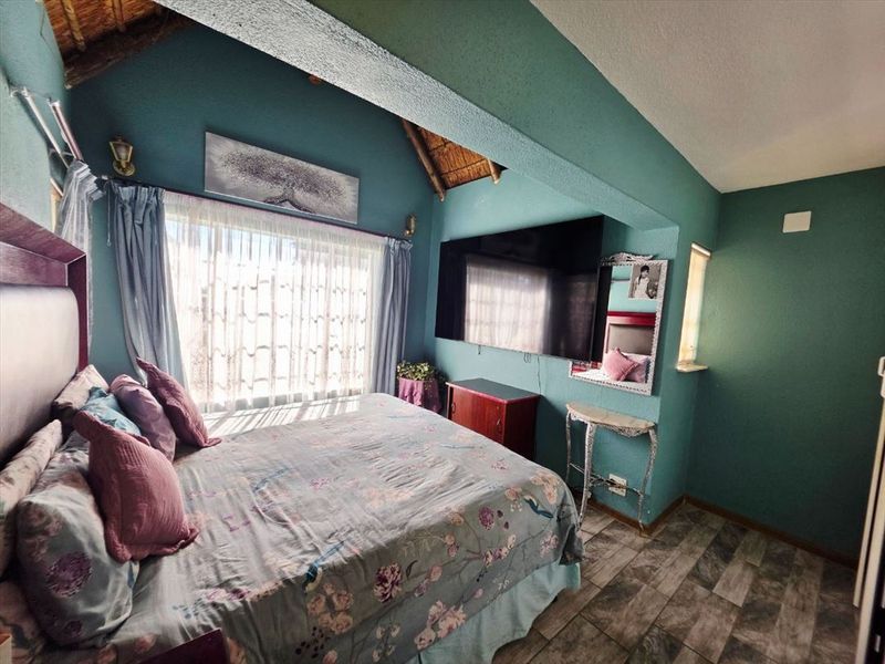 A bedroom featuring a vaulted ceiling with exposed thatch, tiled flooring, and a wall-mounted television.