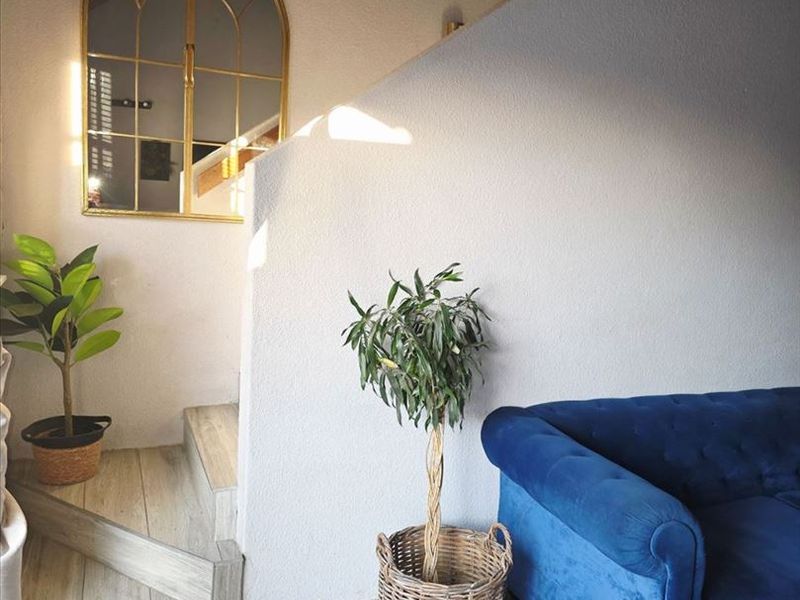 A bright living area featuring modern wood-look tiled flooring and a staircase leading to an upper level, accented by an elegant arched wall mirror.
