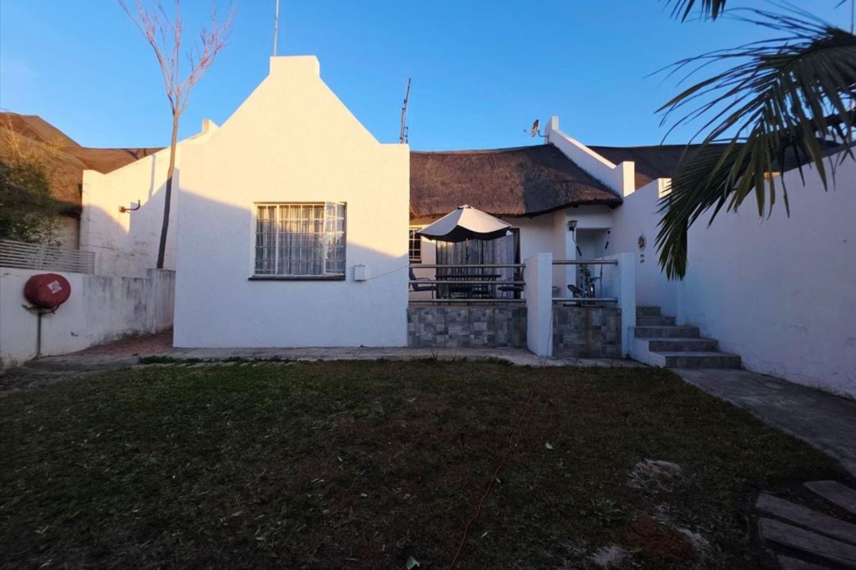 Rear view of a townhouse featuring a thatched roof, a raised patio area with stone cladding, and a private garden space.