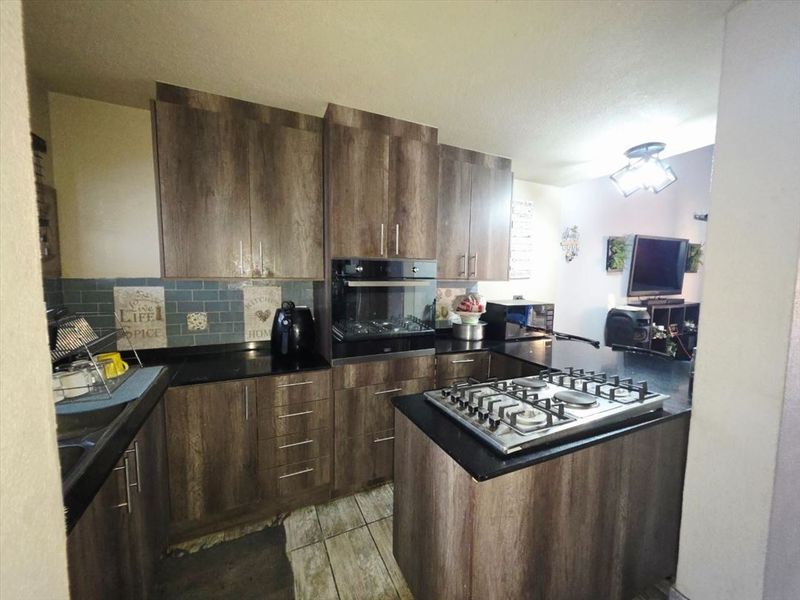 A functional kitchen featuring wood-look cabinetry, granite countertops, a gas hob, and a built-in oven, with an open-plan layout connecting to the living area.