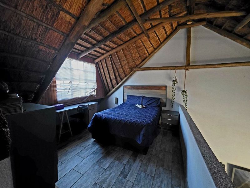 A cozy loft-style bedroom featuring a unique thatched roof with exposed timber rafters, tiled flooring, and a built-in desk area.