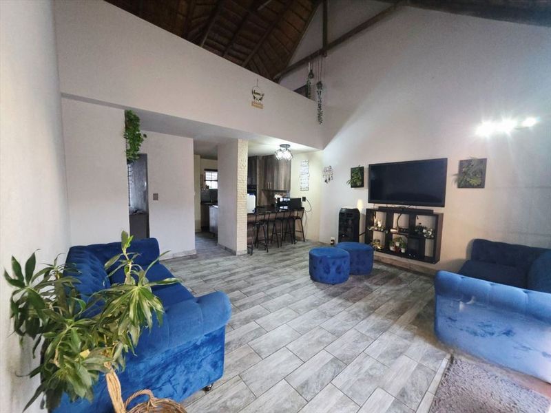 Spacious open-plan living area featuring a high vaulted ceiling with exposed timber rafters and modern tiled flooring, seamlessly connecting to the kitchen.