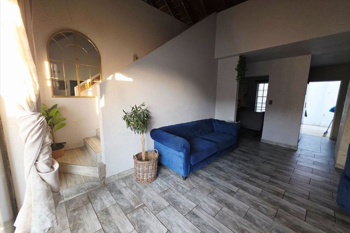 Spacious living area featuring modern wood-look tiled flooring, a staircase, and exposed timber roof beams, offering a bright and open atmosphere.