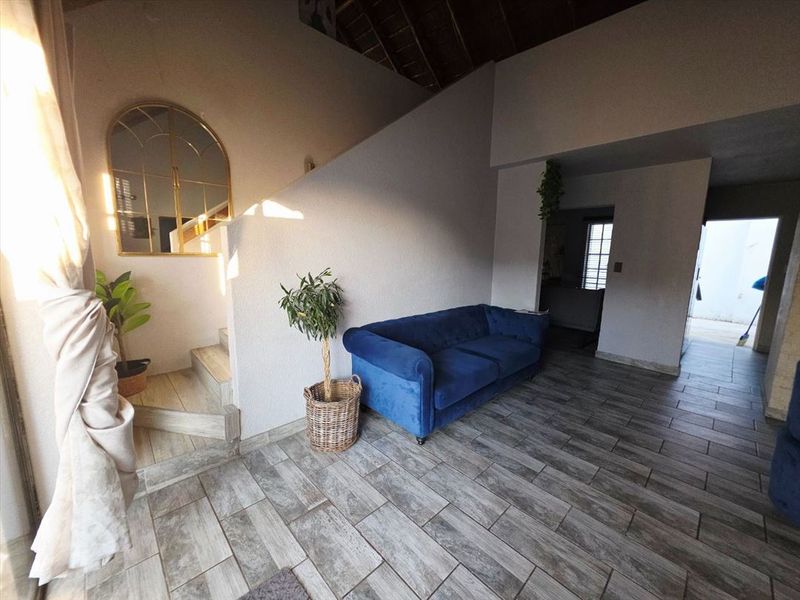 Spacious living area featuring modern wood-look tiled flooring, a staircase, and exposed timber roof beams, offering a bright and open atmosphere.
