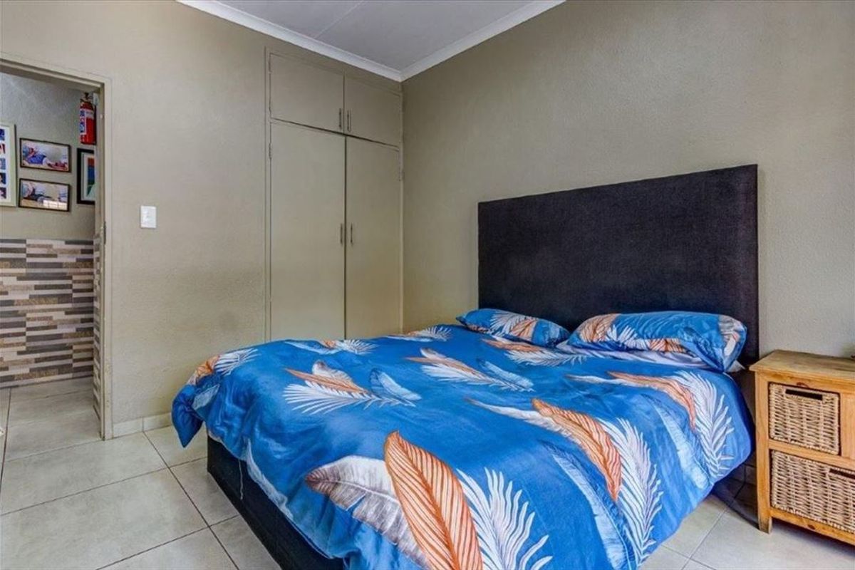 A functional bedroom featuring built-in cupboards, tiled flooring, and neutral wall finishes, providing a practical space with direct access to an adjacent area.