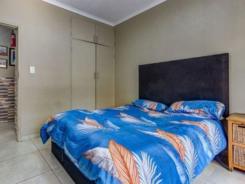 A functional bedroom featuring built-in cupboards, tiled flooring, and neutral wall finishes, providing a practical space with direct access to an adjacent area.
