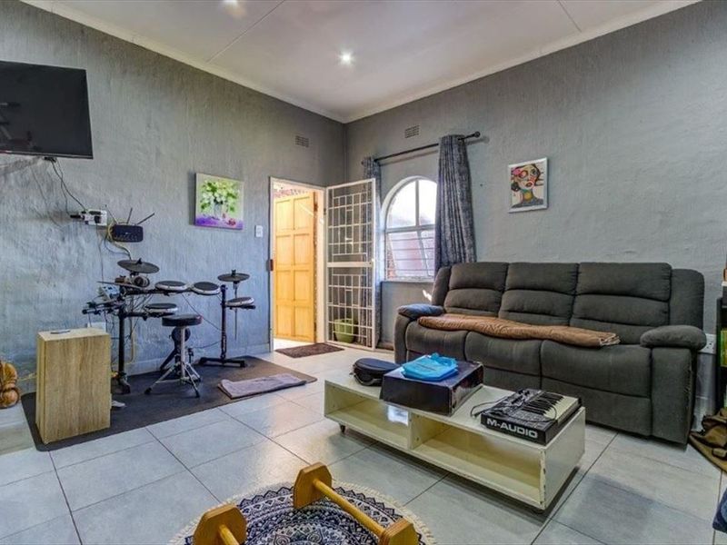 A living room featuring tiled flooring, an arched window with security gate, and recessed ceiling lighting, providing a functional space for relaxation.