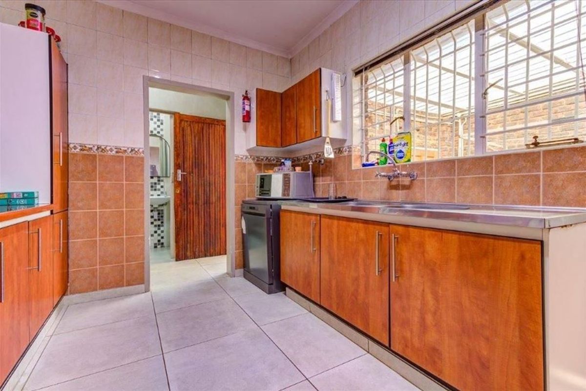 A functional kitchen featuring laminate cabinetry, tiled splashbacks, and a stainless steel sink, with a doorway leading to an adjacent bathroom area.