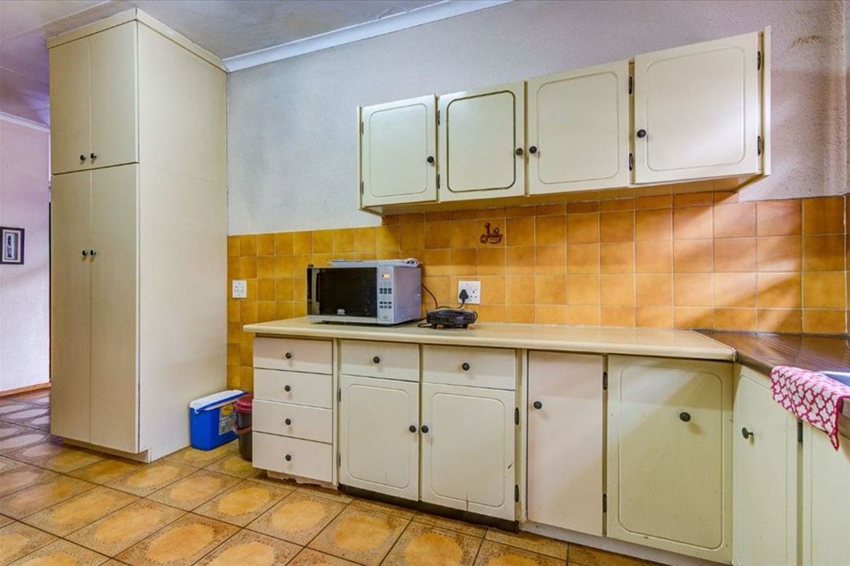 A dated kitchen featuring original cabinetry, tiled backsplash, and tiled flooring, offering significant potential for a modern renovation and aesthetic update.