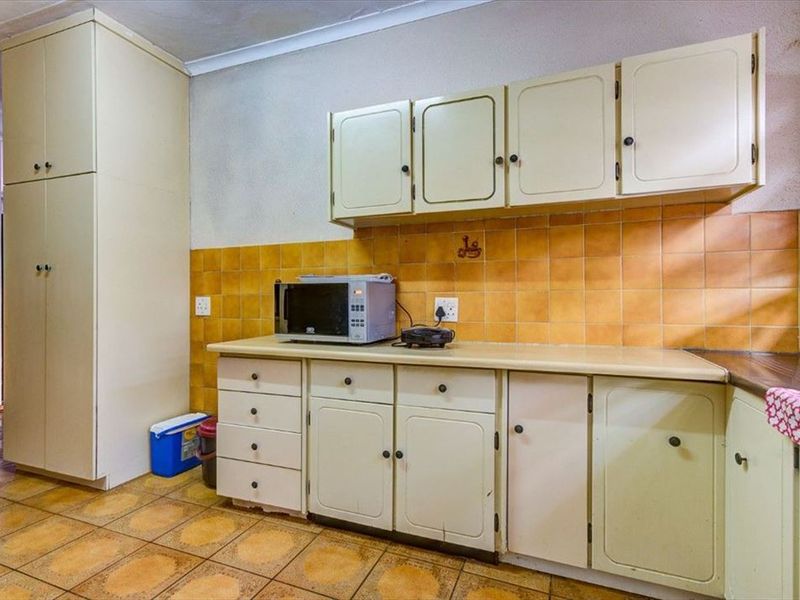 A dated kitchen featuring original cabinetry, tiled backsplash, and tiled flooring, offering significant potential for a modern renovation and aesthetic update.