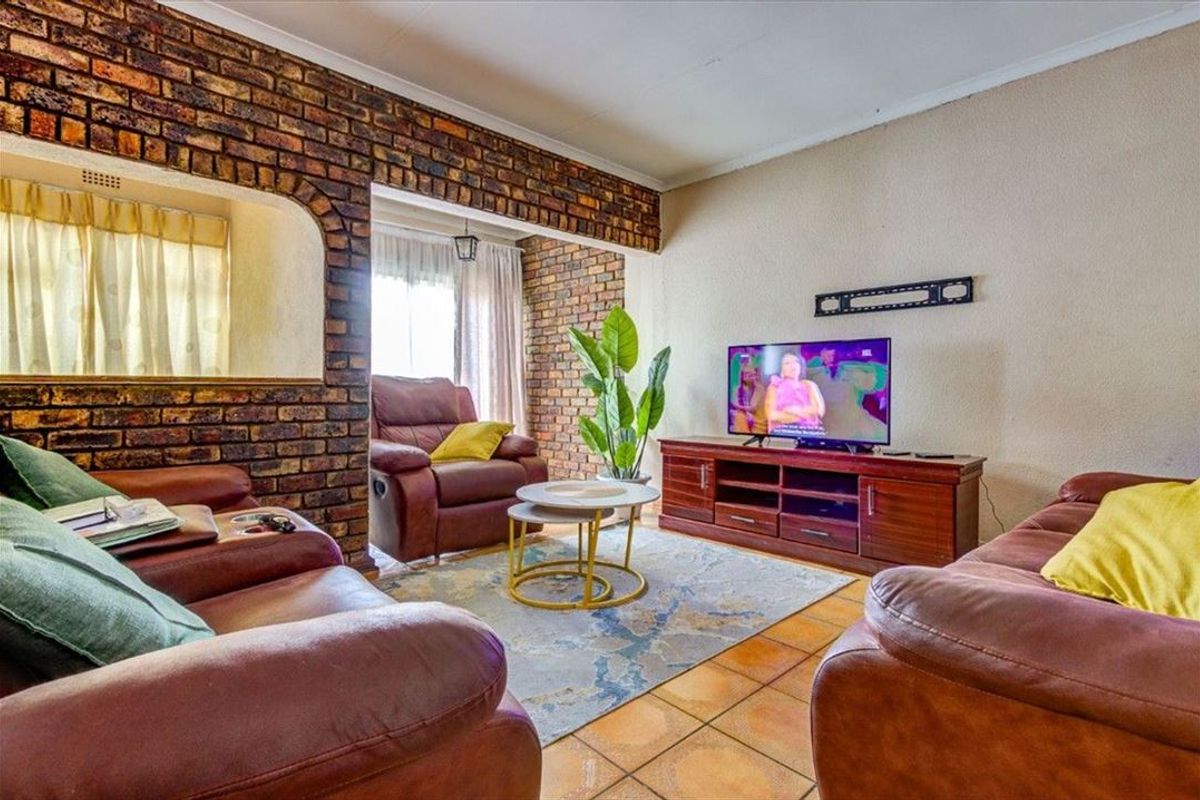 A living room featuring an exposed brick feature wall, ceramic floor tiles, and an arched opening leading to an adjacent space.