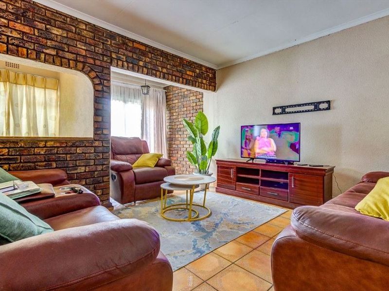 A living room featuring an exposed brick feature wall, ceramic floor tiles, and an arched opening leading to an adjacent space.