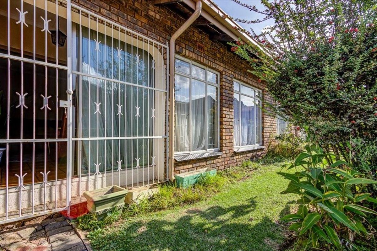 Rear exterior view of the townhouse featuring face brick walls, security gates, and security bars over the windows, adjacent to a small garden area.