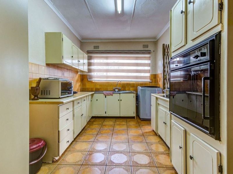 A dated kitchen featuring original cabinetry, tiled backsplash, and tiled flooring, offering significant potential for modernization and renovation.