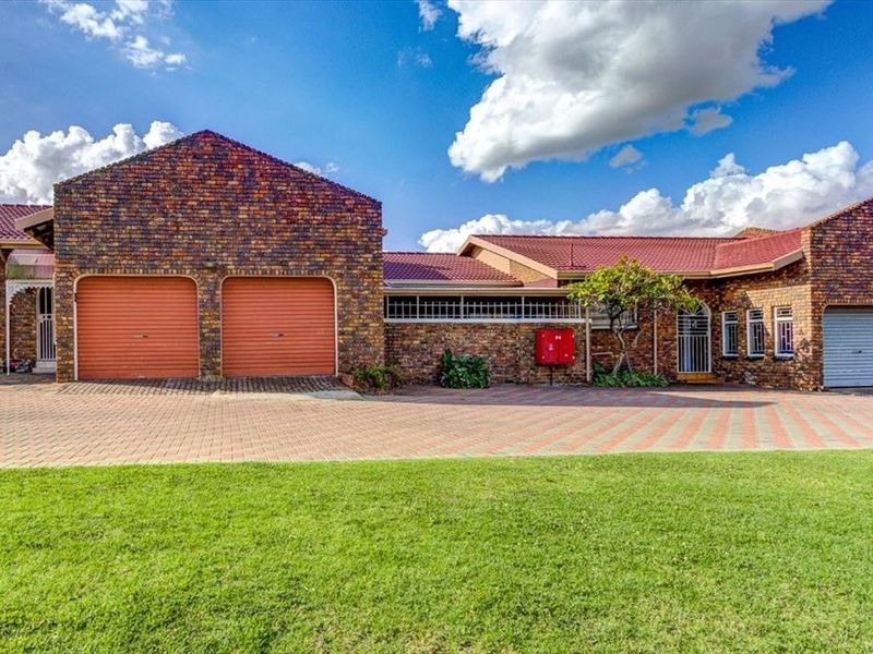 Front exterior view of a townhouse featuring a facebrick facade, tiled roof, multiple garages, and a paved driveway with a well-maintained lawn.