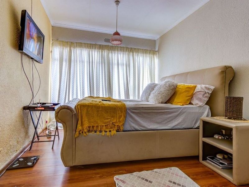 A bedroom featuring laminate flooring and large windows with curtains, providing natural light. The space offers a functional layout for a comfortable sleeping area.