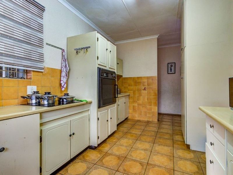 A dated kitchen featuring original cabinetry, built-in oven, ceramic hob, and tiled finishes throughout, offering significant potential for a modern renovation.