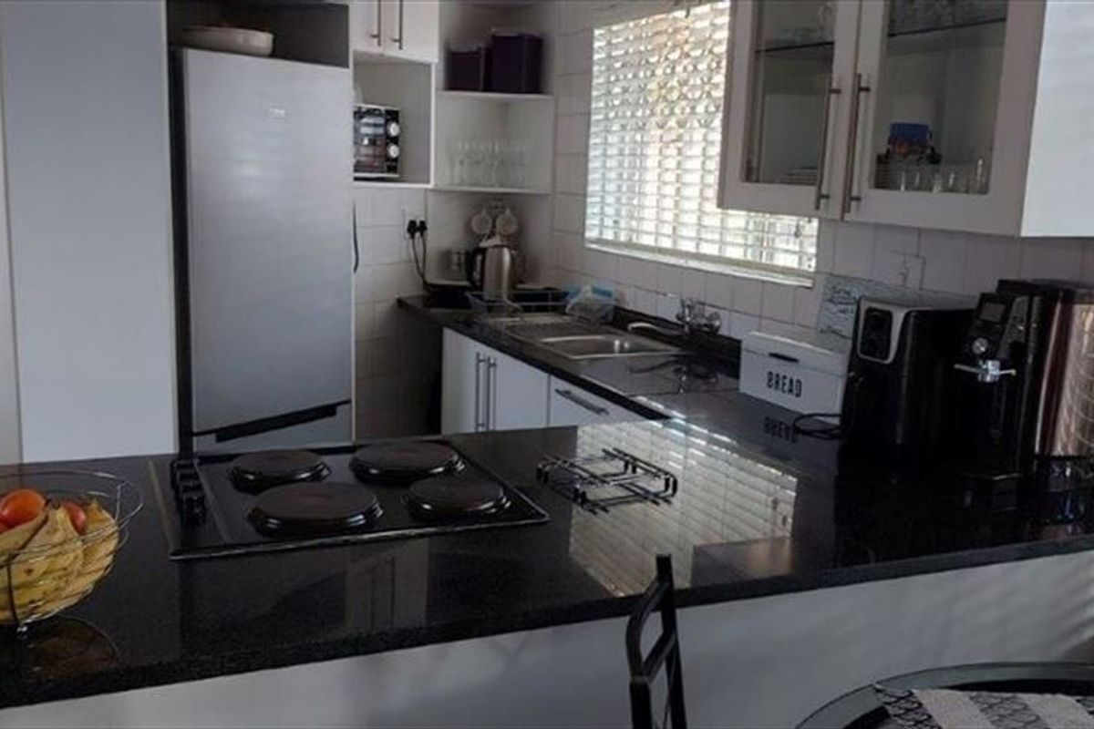 A functional kitchen featuring granite countertops, an electric hob, built-in cabinetry, and a tiled backsplash with natural light from the window.